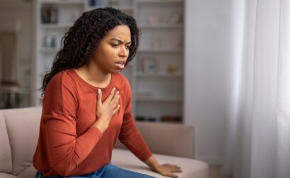 Concerned young black woman suffering pain in chest while sitting on couch