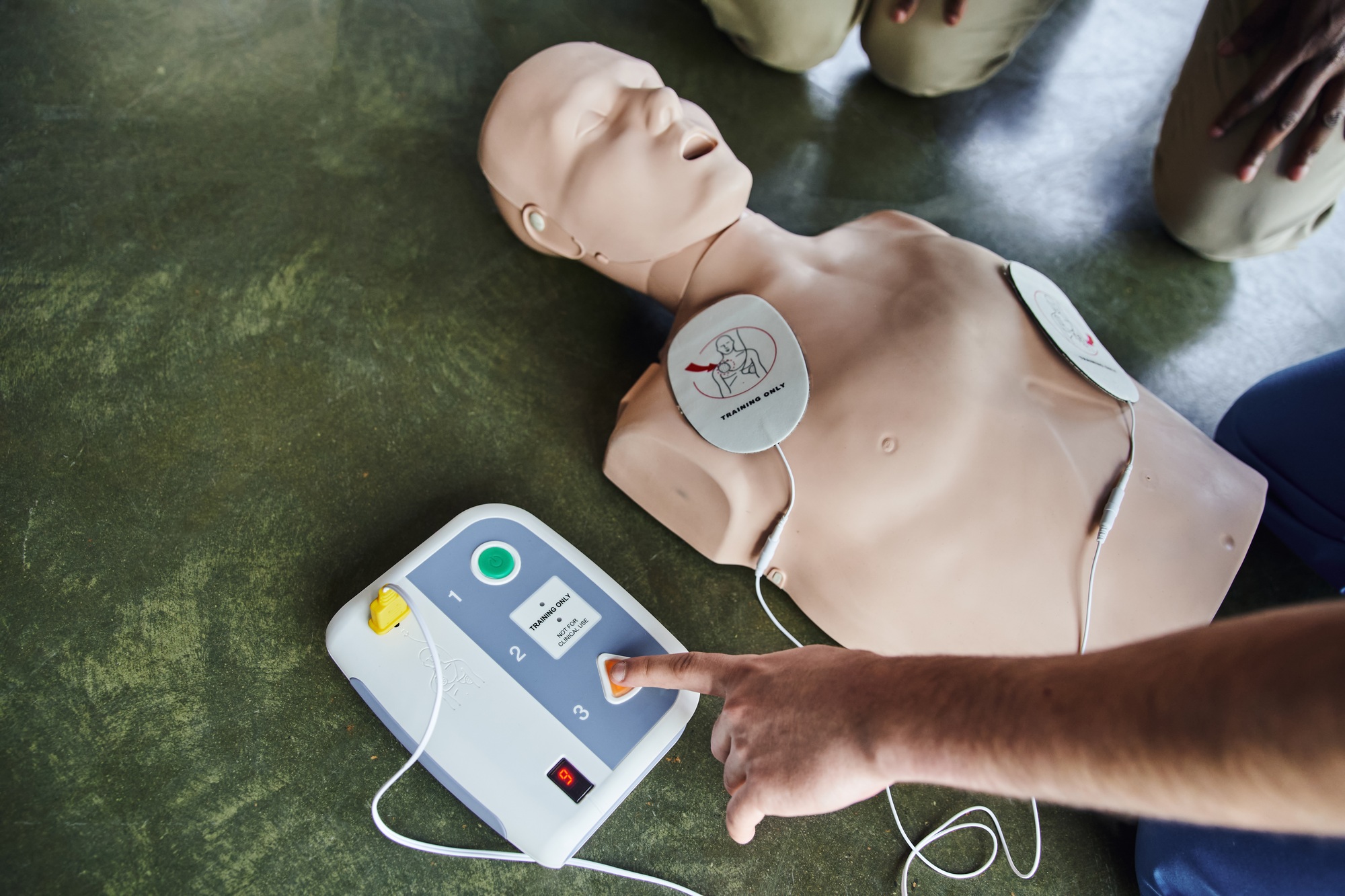 partial view of professional medical instructor operating defibrillator on CPR manikin near young