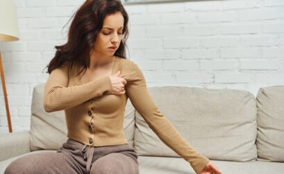 Young brunette woman in brown jumper suffering from pain while massaging lymphatic nodes on armpit